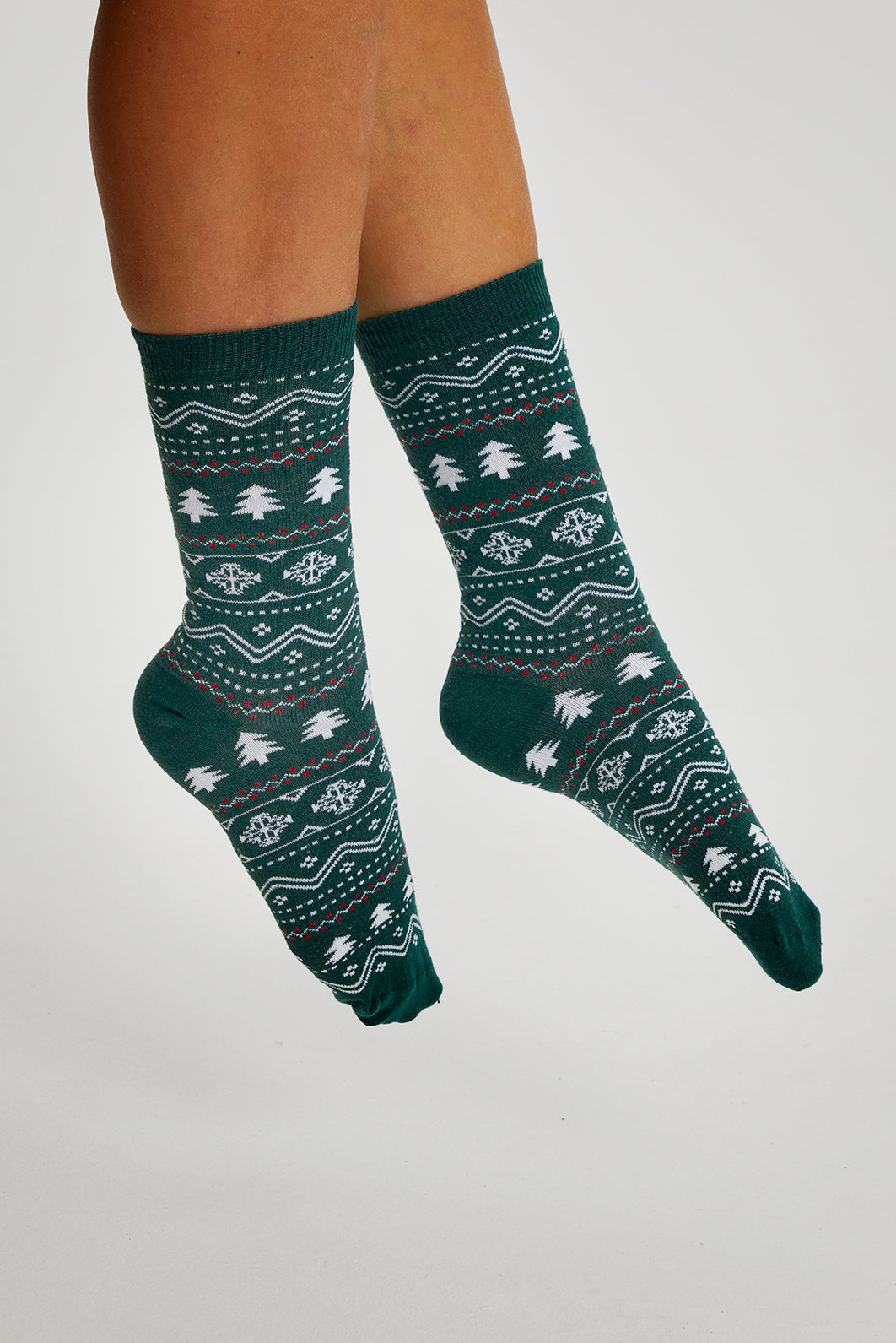 Een paar benen met een paar groene kerstsokken met kerstbomen erop.