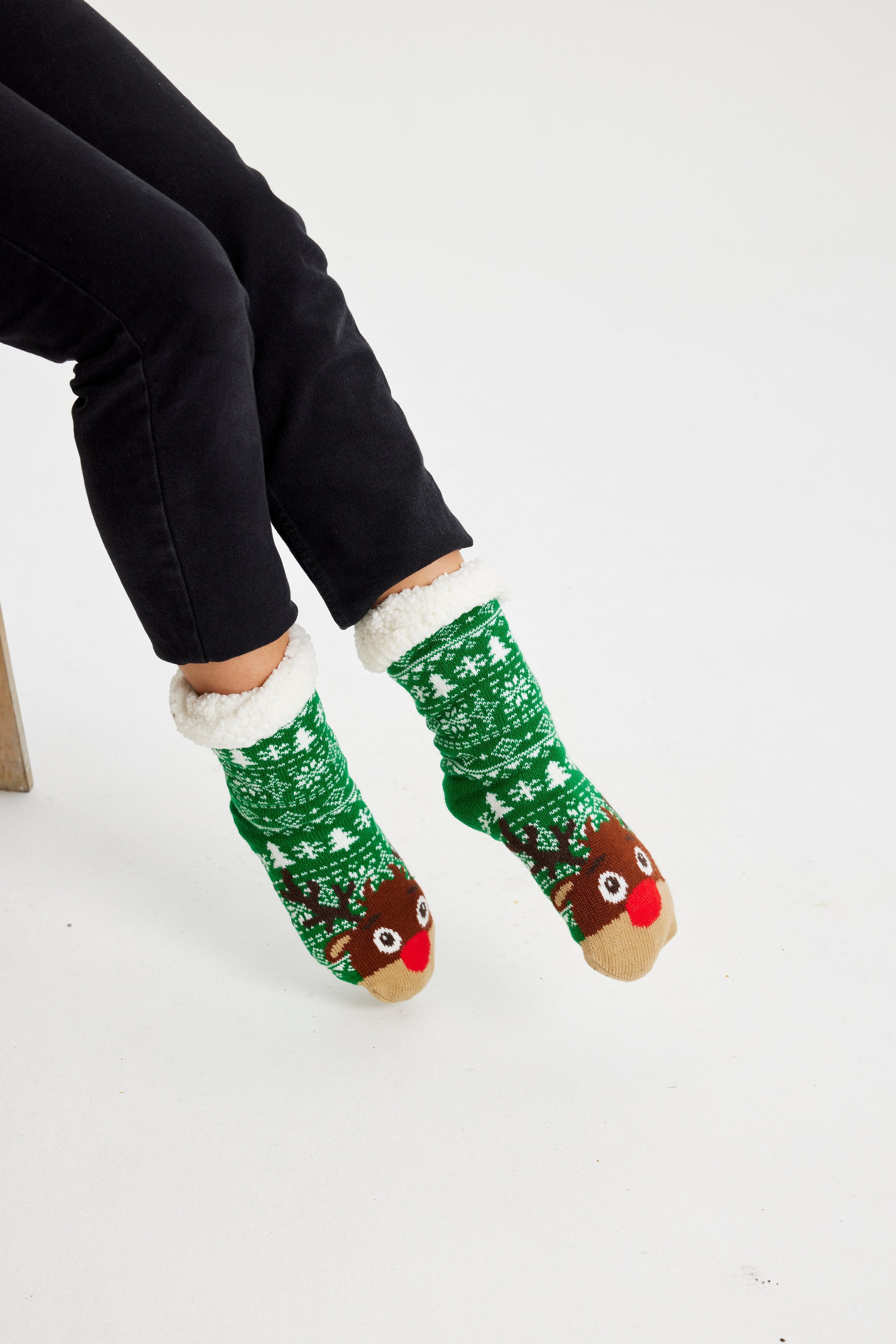 Een paar benen met groene kerstsokken met een rendier erop.